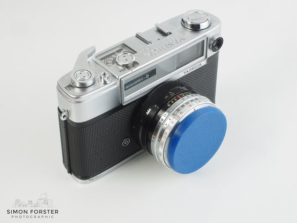 A Red 3d printed front cap that has been fitted onto a Rollei XF 35 camera lens, being showcased with a plain white background