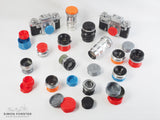 All varients of forster uk's CRF or nikon S mount rear lens caps and contax and kiev body caps are being displayed on a plain white background. The caps are in a range of colours such as black, orange, red, mid blue, silver and survival green. Been displayed for the purpose of showing the caps function, a range of lenses and cameras are showcasing the caps. The rear caps are suitable for carl zeiss sonnar and jupiter 8, 3 lenses etc.