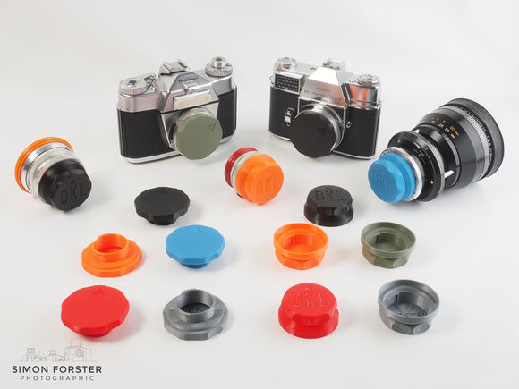 A rear lens cap for DKL Schneider is being displayed in black, orange, red, mid blue and survival green. There are also body caps for DKL schneider being displayed in these colours.